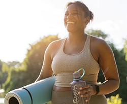 Woman smiling while holding workout mat and water bottle