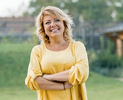 Woman in yellow shirt smiling with her arms crossed while outside