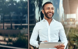 a confident young businessperson smiling and standing in front of a building