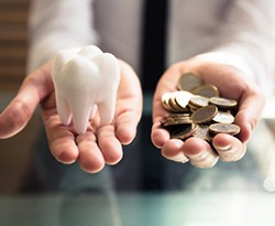 hands holding a tooth and coins representing the cost of cosmetic dentistry in Lincoln 