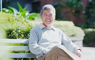 A man sitting on a bench and smiling after receiving his dental implants in Lincoln