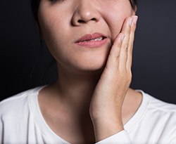 woman with hand on jaw after getting dental implants in Lincoln