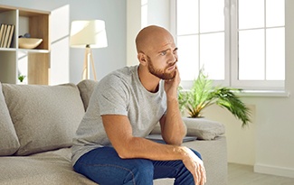Bearded man rubbing jaw and sitting on couch