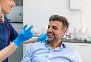 Smiling dental assistant holding clear aligner with patient