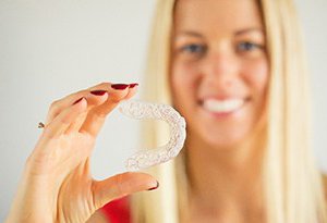 A young woman holding a clear Invisalign aligner in her right hand
