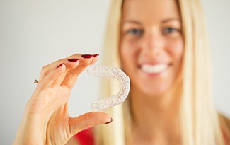 A young woman holding a clear Invisalign aligner in her right hand