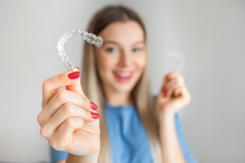 a woman smiling while holding Invisalign aligners